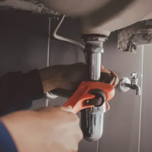 A close-up of hands using a wrench to tighten or adjust a chrome sink drain pipe under a bathroom sink.