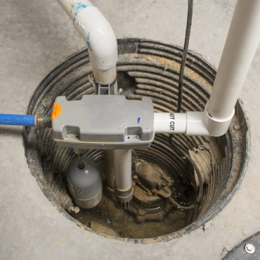 A sump pump system installed in a sump pit, featuring a pump, pipes, and a control unit, with water at the bottom of the pit.